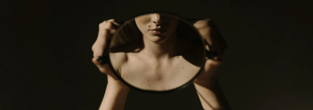 Vrouw die in de spiegel kijkt – op het punt van eerlijke zelfreflectie. Klaar om haar gedachten, gevoelens en gedrag onder de loep te nemen.