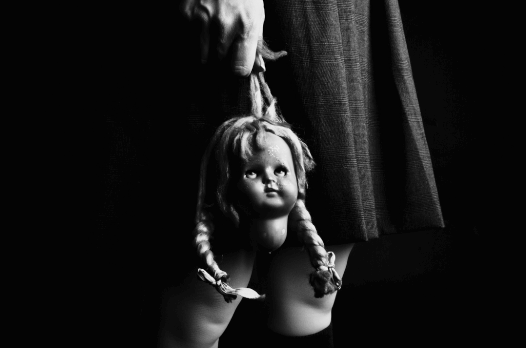 Een volwassen hand die de kop van een pop vasthoudt, symboliseert hoe vroege kindertijd-imprints onze diepgewortelde patronen vormen. De basis van oud gedrag.